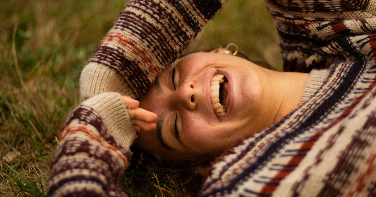 vrouw ligt in het gras en lacht naar de camera