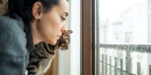 vrouw kijkt met kat somber door slecht weer naar buiten