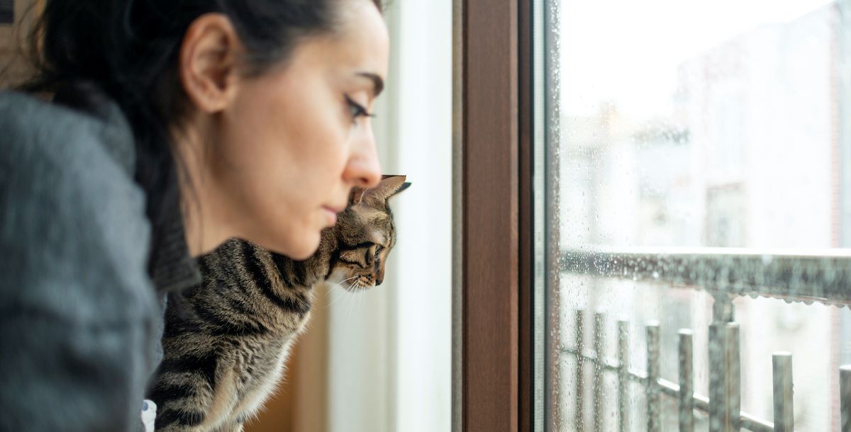 vrouw kijkt met kat somber door slecht weer naar buiten