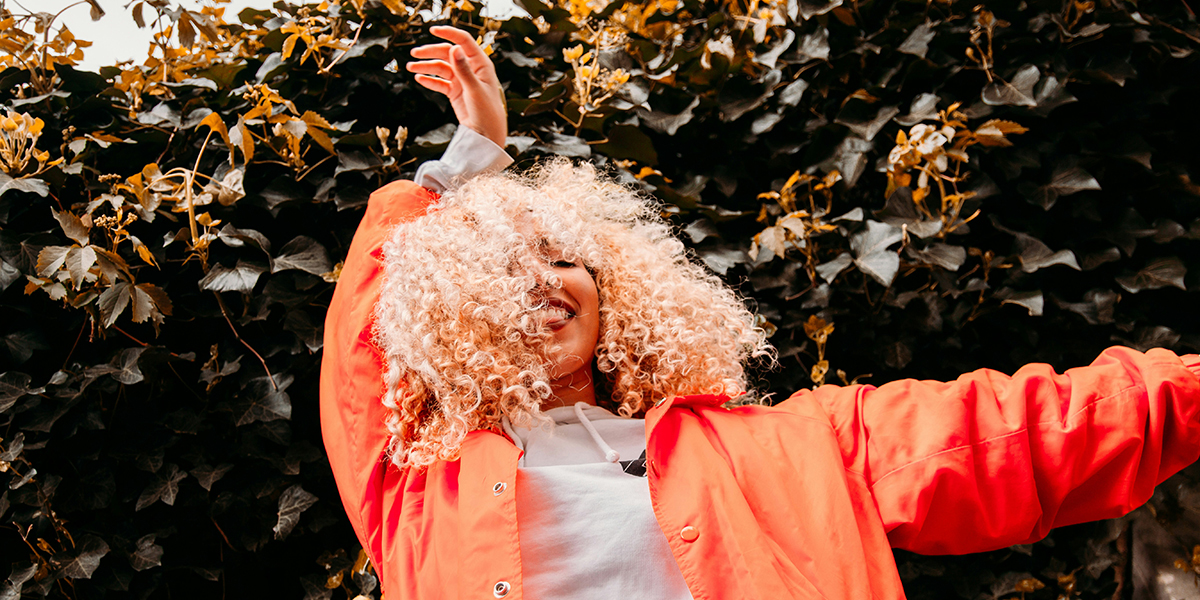 Een blije zelfverzekerde vrouw met een oranje jas en krullend haar