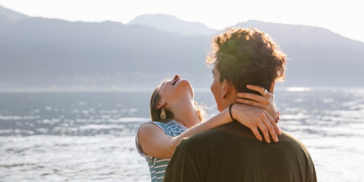 Een man en een vrouw die in elkaars armen vallen bij een meer en duidelijk verliefd zijn.