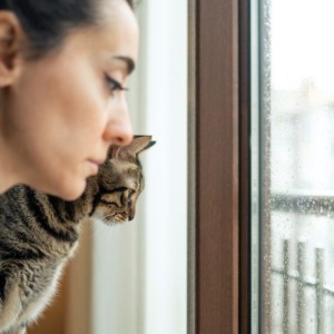 vrouw kijkt met kat somber door slecht weer naar buiten