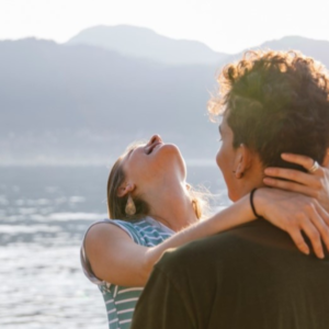 Een man en een vrouw die in elkaars armen vallen bij een meer en duidelijk verliefd zijn.